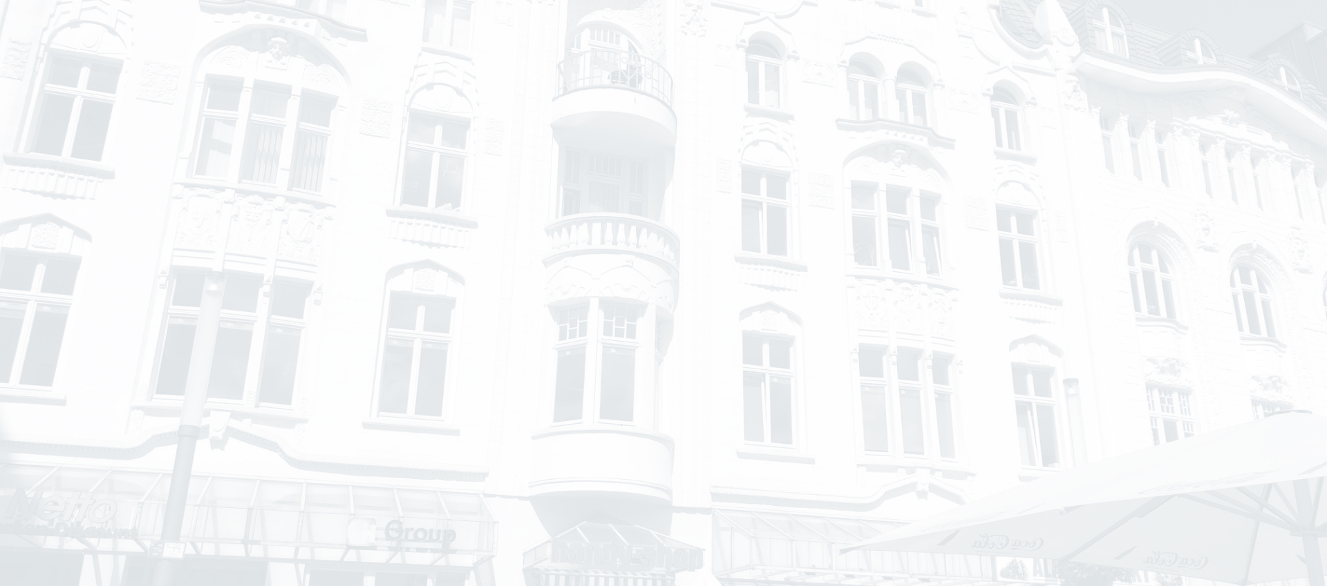 Das Hintergrundbild zeigt die Fassade eines schwarz-weiß gefärbten Wohn- und Geschäftshaus.